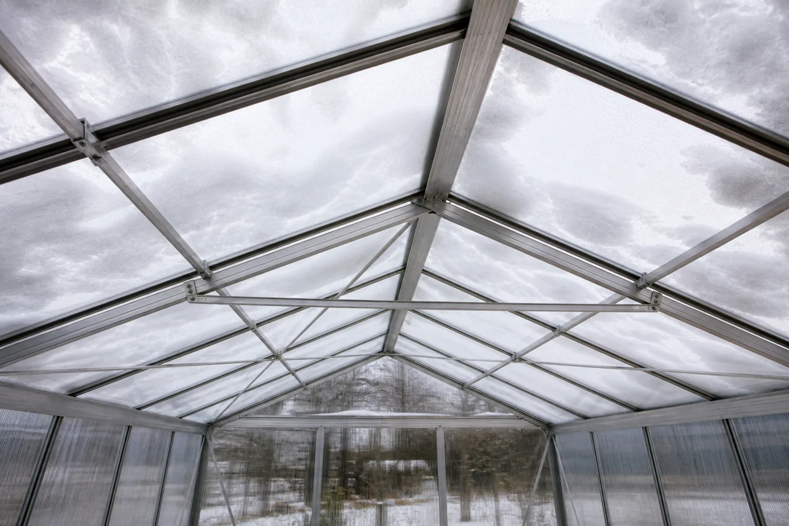 Interior view of greenhouse rafters, purlins, and cross bracing beneath a snow-covered roof